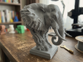 Buste d’éléphant sculpté gris, vue inclinée avec trompe et oreille visibles.